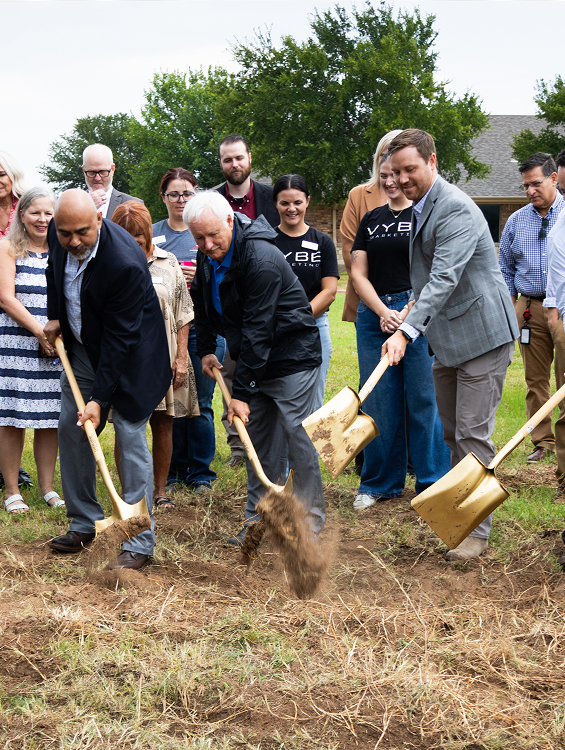 Group of people breaking ground at a site with gold shovels